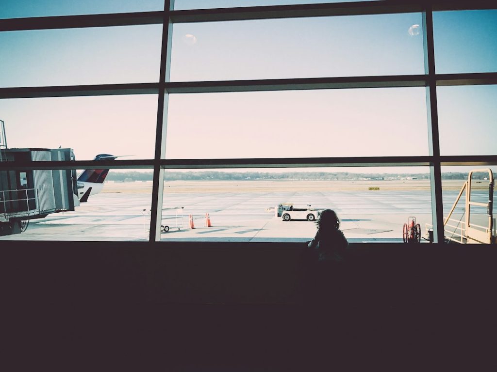 Traveler looking out of an airport window at a plane, planning an international trip